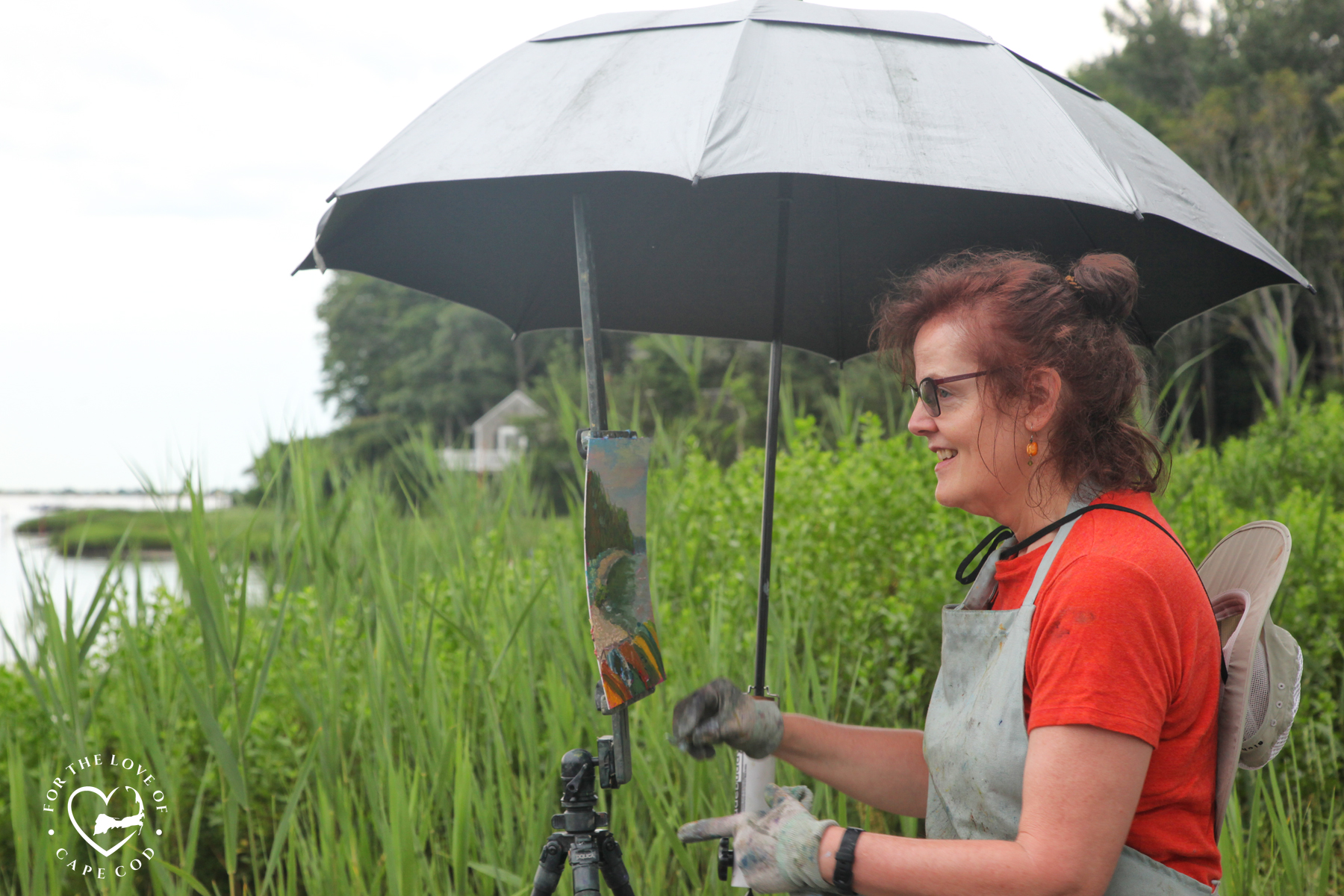 Karen painting under a silver umbrella with a background of tall beach grass